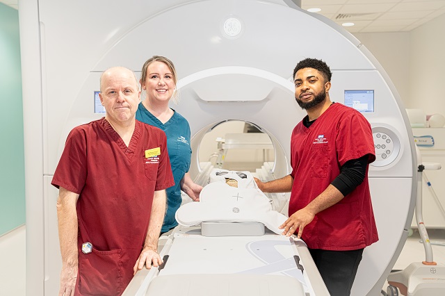 Three uniformed healthcare staff stand around a scanner