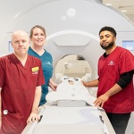 Three uniformed healthcare staff stand around a scanner