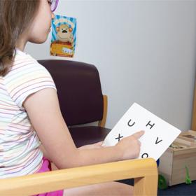 Child holding a letter card and pointing at the letter H