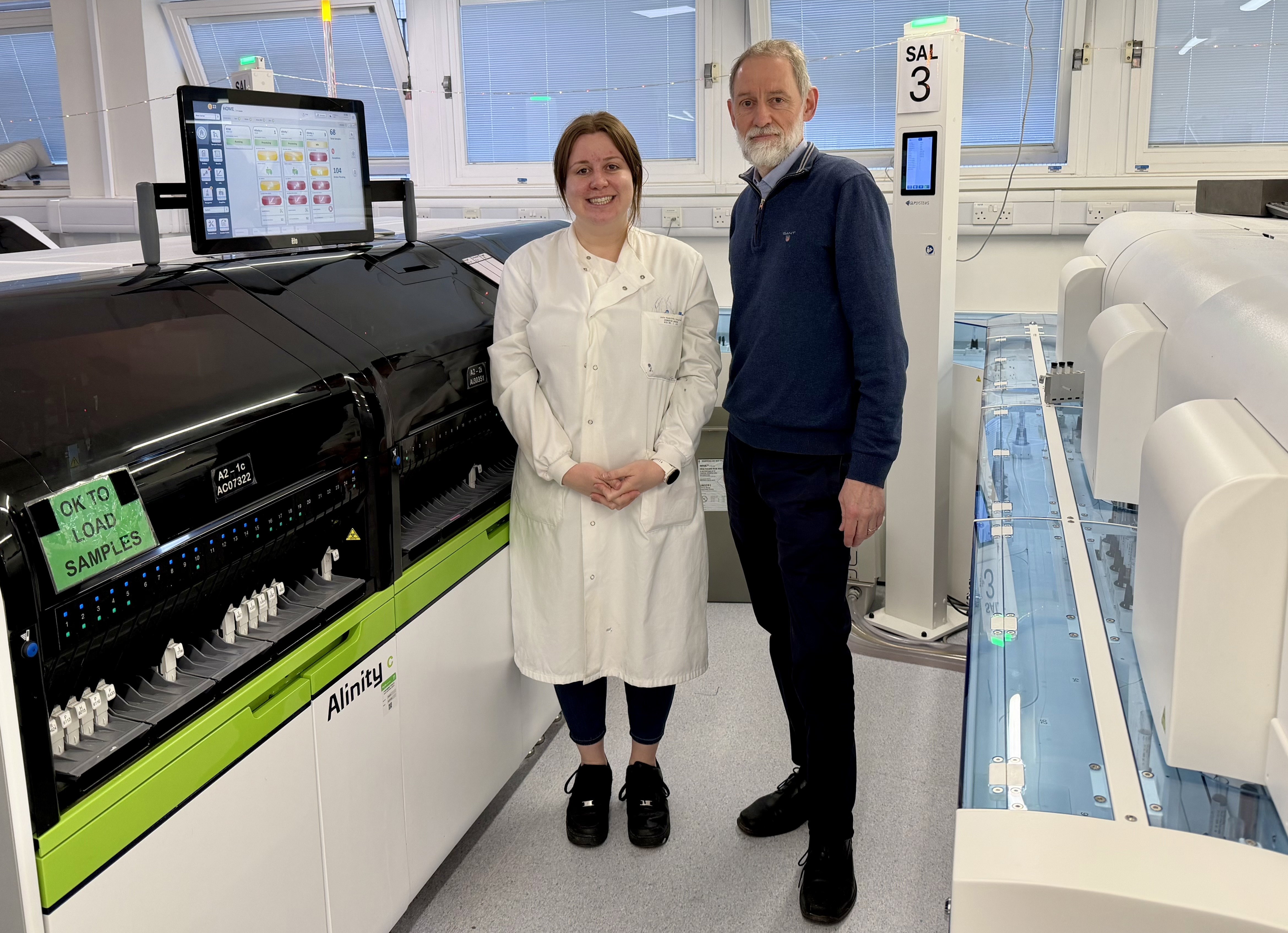 Man and woman stand in laboratory in front of analyser machine