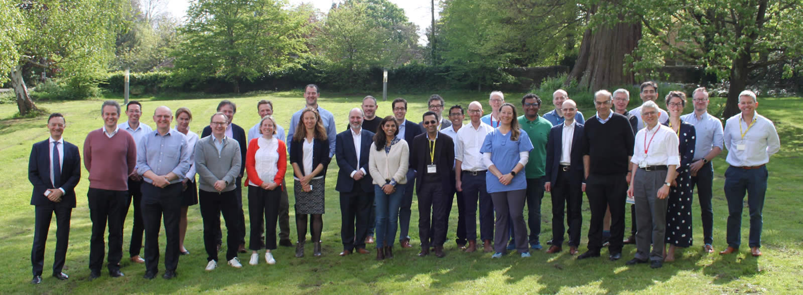 31 smiling men and women lined up in a sunlit garden