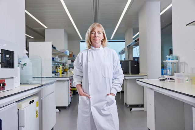 Professor Sarah Blagden standing in a modern laboratory setting, in a lab coat