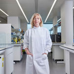 Professor Sarah Blagden standing in a modern laboratory setting, in a lab coat