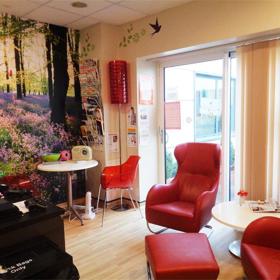 Room with mural of forest on wall. Contains easy chairs, foot stool and side tables.