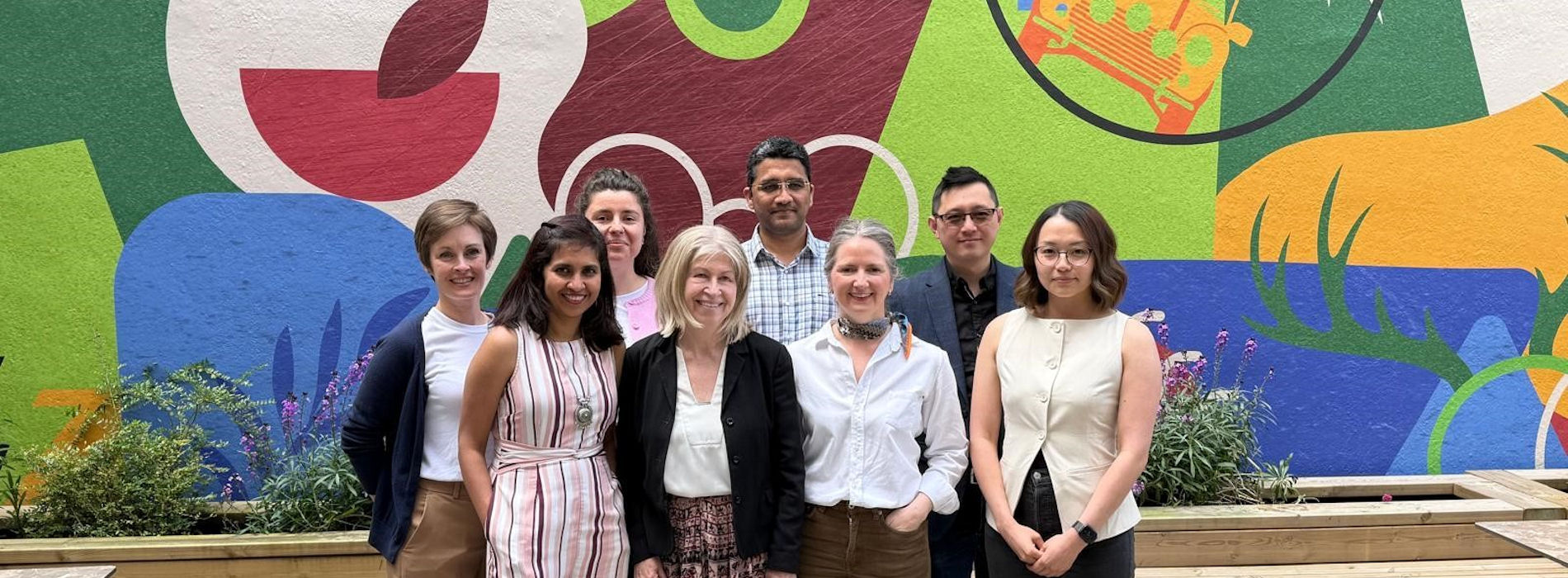 Eight people standing in front of a bright mural
