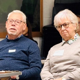 An older man and woman seated, with name stickers on their jumpers.