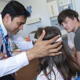 A consultant examines the head of a young girl in a clinic room.
