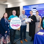 Seven people in front of a screen that says 'AccessAble'. Two people hold a plaque that celebrates the launch of the new guides. Two people wear 'Oxford Hospitals Charity' branded t-shirts, while one holds a banner that has the same name.