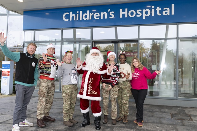 Santa, wearing his traditional red suit, is joined by four people wearing military uniform and Christmas jumpers and two others wearing Oxford Hospitals Charity jumpers. There is a hospital 'Children's Hospital' sign in the background