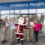 Santa, wearing his traditional red suit, is joined by four people wearing military uniform and Christmas jumpers and two others wearing Oxford Hospitals Charity jumpers. There is a hospital 'Children's Hospital' sign in the background