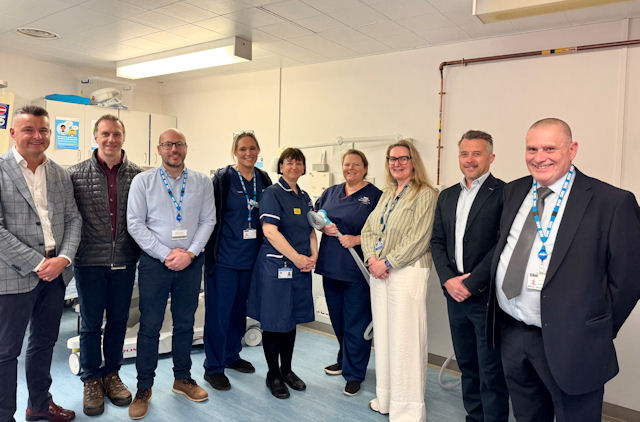 Nine smiling people, some in scrubs, others in office wear, in a clinical setting