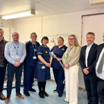Nine smiling people, some in scrubs, others in office wear, in a clinical setting