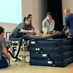 Five people on a stage lift a dummy on to a pile of stretchers