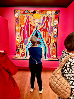 A short woman seen from behind as she looks at a large vibrant modern painting in a gallery