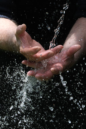 Two hands held under running water, plain dark background