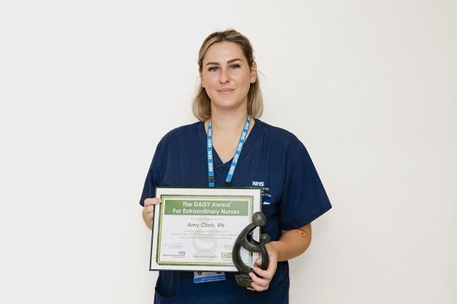 Amy Clark holding DAISY certificate and a hand-carved sculpture - 'A Healer's Touch'
