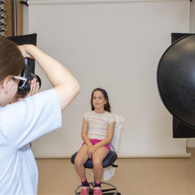 A photographer takes a picture of a young person sitting close by.