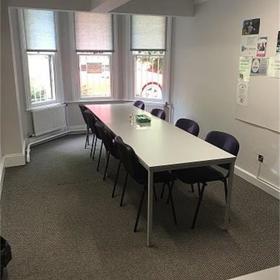 Long table with nine chairs in neat room: sunshine through bay window.