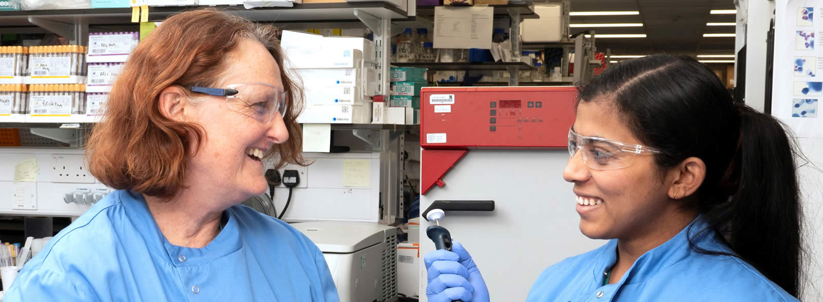 Two smiling women in scrubs converse in a laboratory