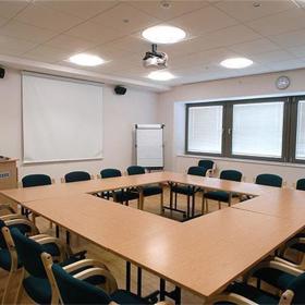 Inside a meeting room set up in boardroom style, with several tables put together to make one.
