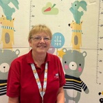 Sheila wearing her red 'play' uniform and in front of children's hospital play resources