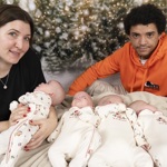 Mum and dad with their quadruplets, who are lying down and wearing matching Christmas outfits. There is a festive display in the background